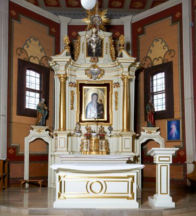 Zdjęcie nr 1: Ołtarz architektoniczny, drewniany, jednoosiowy, jednokondygnacyjny z bramkami. Mensa wąska, prostopadłościenna o ściankach wklęsło-wypukłych. Tabernakulum w kształcie prostopadłościennej skrzynki z przodu o linii wklęsło-wypukłej z uskokami. Ustawione jest na  wysokim cokole, flankowane parą szerokich, wklęsłych pilastrów, zdobionych ornamentem złożonym z przeplatających się wolut i kampanul. Ścianka frontowa wypukła, w polu prostokątne, metalowe drzwiczki, zdobione kiśćmi winogron i kłosami zbóż, pośrodku łaciński prosty krzyż. Całość zamknięta profilowanym gzymsem. Po bokach tabernakulum zwisy z kampanul, a na skrajach płaskorzeźbione uszy z liści akantu.  Do górnej krawędzi przybite gwoździem na trzech tulejach lampki oliwne. Nad tabernakulum tron wystawienia z rzeźbionymi w drewnie aniołkami na obłokach adorującymi krucyfiks. 

Retabulum ustawione na zdwojonym cokole, ujęte zwielokrotnionymi pilastrami toskańskimi i dwiema kolumnami kompozytowymi na wysokich cokołach, ustawionymi pod kątem i podtrzymującymi profilowane, przerwane belkowanie. Pilastry od strony wewnętrznej ołtarza są wklęsłe, ozdobione dwiema parami uskrzydlonych główek anielskich i zwisami z kwiatów; od zewnątrz pilastry mają trzony wypukłe.  W polu głównym wnęka, ujęta ramą w kształcie stojącego prostokąta o uszatych narożach. We wnęce na czerwonym tle umieszczony obraz Matki Boskiej Piekarskiej, na zasuwach obrazy „Koronacja Matki Boskiej” oraz „Św. Mikołaj”. Nad obrazem kartusz o kształcie zbliżonym do rombu z ornamentami rocaille&#039;owymi wokół; w polu napis „ALTARE / PRIVILEGI/ATUM”. Na osi kolumn, na przyczółku ustawione są wazony z kwiatami. 

Zwieńczenie w kształcie stojącego prostokąta, flankowane parą pilastrów podtrzymujących przerwane belkowanie, zamknięte gzymsem w formie łuku odcinkowego. Na szczycie promienista gloria z otokiem chmur pośrodku z płaskorzeźbionym monogramem IHS. W polu głównym obraz przedstawiający Ekstazę św. Teresy w kształcie stojącego prostokąta, zamknięty łukiem nadwieszonym. Po bokach zwieńczenia uszy z liści akantu i kwiatów. Pod obrazem uskrzydlona para główek aniołków. 

Bramki w formie stojącego prostokąta, flankowane węgarami, zamknięte wolutowym łukiem z ustawionymi na szczycie na niskich cokołach rzeźbami świętych: po lewej św. Piotra, a po prawej św. Pawła.  Przejście zamknięte łukiem wklęsło-wypukłym z uskokami. Struktura polichromowana w kolorze jasnobeżowym, ornamentyka złocona, detale srebrzone.
