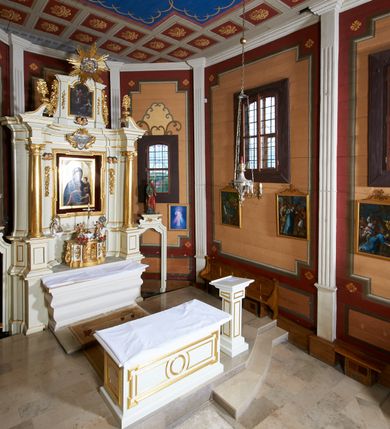 Zdjęcie nr 20: Ołtarz architektoniczny, drewniany, jednoosiowy, jednokondygnacyjny z bramkami. Mensa wąska, prostopadłościenna o ściankach wklęsło-wypukłych. Tabernakulum w kształcie prostopadłościennej skrzynki z przodu o linii wklęsło-wypukłej z uskokami. Ustawione jest na  wysokim cokole, flankowane parą szerokich, wklęsłych pilastrów, zdobionych ornamentem złożonym z przeplatających się wolut i kampanul. Ścianka frontowa wypukła, w polu prostokątne, metalowe drzwiczki, zdobione kiśćmi winogron i kłosami zbóż, pośrodku łaciński prosty krzyż. Całość zamknięta profilowanym gzymsem. Po bokach tabernakulum zwisy z kampanul, a na skrajach płaskorzeźbione uszy z liści akantu.  Do górnej krawędzi przybite gwoździem na trzech tulejach lampki oliwne. Nad tabernakulum tron wystawienia z rzeźbionymi w drewnie aniołkami na obłokach adorującymi krucyfiks. 

Retabulum ustawione na zdwojonym cokole, ujęte zwielokrotnionymi pilastrami toskańskimi i dwiema kolumnami kompozytowymi na wysokich cokołach, ustawionymi pod kątem i podtrzymującymi profilowane, przerwane belkowanie. Pilastry od strony wewnętrznej ołtarza są wklęsłe, ozdobione dwiema parami uskrzydlonych główek anielskich i zwisami z kwiatów; od zewnątrz pilastry mają trzony wypukłe.  W polu głównym wnęka, ujęta ramą w kształcie stojącego prostokąta o uszatych narożach. We wnęce na czerwonym tle umieszczony obraz Matki Boskiej Piekarskiej, na zasuwach obrazy „Koronacja Matki Boskiej” oraz „Św. Mikołaj”. Nad obrazem kartusz o kształcie zbliżonym do rombu z ornamentami rocaille'owymi wokół; w polu napis „ALTARE / PRIVILEGI/ATUM”. Na osi kolumn, na przyczółku ustawione są wazony z kwiatami. 

Zwieńczenie w kształcie stojącego prostokąta, flankowane parą pilastrów podtrzymujących przerwane belkowanie, zamknięte gzymsem w formie łuku odcinkowego. Na szczycie promienista gloria z otokiem chmur pośrodku z płaskorzeźbionym monogramem IHS. W polu głównym obraz przedstawiający Ekstazę św. Teresy w kształcie stojącego prostokąta, zamknięty łukiem nadwieszonym. Po bokach zwieńczenia uszy z liści akantu i kwiatów. Pod obrazem uskrzydlona para główek aniołków. 

Bramki w formie stojącego prostokąta, flankowane węgarami, zamknięte wolutowym łukiem z ustawionymi na szczycie na niskich cokołach rzeźbami świętych: po lewej św. Piotra, a po prawej św. Pawła.  Przejście zamknięte łukiem wklęsło-wypukłym z uskokami. Struktura polichromowana w kolorze jasnobeżowym, ornamentyka złocona, detale srebrzone.
