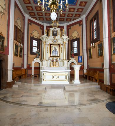 Zdjęcie nr 2: Ołtarz architektoniczny, drewniany, jednoosiowy, jednokondygnacyjny z bramkami. Mensa wąska, prostopadłościenna o ściankach wklęsło-wypukłych. Tabernakulum w kształcie prostopadłościennej skrzynki z przodu o linii wklęsło-wypukłej z uskokami. Ustawione jest na  wysokim cokole, flankowane parą szerokich, wklęsłych pilastrów, zdobionych ornamentem złożonym z przeplatających się wolut i kampanul. Ścianka frontowa wypukła, w polu prostokątne, metalowe drzwiczki, zdobione kiśćmi winogron i kłosami zbóż, pośrodku łaciński prosty krzyż. Całość zamknięta profilowanym gzymsem. Po bokach tabernakulum zwisy z kampanul, a na skrajach płaskorzeźbione uszy z liści akantu.  Do górnej krawędzi przybite gwoździem na trzech tulejach lampki oliwne. Nad tabernakulum tron wystawienia z rzeźbionymi w drewnie aniołkami na obłokach adorującymi krucyfiks. 

Retabulum ustawione na zdwojonym cokole, ujęte zwielokrotnionymi pilastrami toskańskimi i dwiema kolumnami kompozytowymi na wysokich cokołach, ustawionymi pod kątem i podtrzymującymi profilowane, przerwane belkowanie. Pilastry od strony wewnętrznej ołtarza są wklęsłe, ozdobione dwiema parami uskrzydlonych główek anielskich i zwisami z kwiatów; od zewnątrz pilastry mają trzony wypukłe.  W polu głównym wnęka, ujęta ramą w kształcie stojącego prostokąta o uszatych narożach. We wnęce na czerwonym tle umieszczony obraz Matki Boskiej Piekarskiej, na zasuwach obrazy „Koronacja Matki Boskiej” oraz „Św. Mikołaj”. Nad obrazem kartusz o kształcie zbliżonym do rombu z ornamentami rocaille'owymi wokół; w polu napis „ALTARE / PRIVILEGI/ATUM”. Na osi kolumn, na przyczółku ustawione są wazony z kwiatami. 

Zwieńczenie w kształcie stojącego prostokąta, flankowane parą pilastrów podtrzymujących przerwane belkowanie, zamknięte gzymsem w formie łuku odcinkowego. Na szczycie promienista gloria z otokiem chmur pośrodku z płaskorzeźbionym monogramem IHS. W polu głównym obraz przedstawiający Ekstazę św. Teresy w kształcie stojącego prostokąta, zamknięty łukiem nadwieszonym. Po bokach zwieńczenia uszy z liści akantu i kwiatów. Pod obrazem uskrzydlona para główek aniołków. 

Bramki w formie stojącego prostokąta, flankowane węgarami, zamknięte wolutowym łukiem z ustawionymi na szczycie na niskich cokołach rzeźbami świętych: po lewej św. Piotra, a po prawej św. Pawła.  Przejście zamknięte łukiem wklęsło-wypukłym z uskokami. Struktura polichromowana w kolorze jasnobeżowym, ornamentyka złocona, detale srebrzone.
