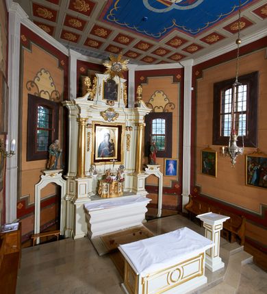 Zdjęcie nr 21: Ołtarz architektoniczny, drewniany, jednoosiowy, jednokondygnacyjny z bramkami. Mensa wąska, prostopadłościenna o ściankach wklęsło-wypukłych. Tabernakulum w kształcie prostopadłościennej skrzynki z przodu o linii wklęsło-wypukłej z uskokami. Ustawione jest na  wysokim cokole, flankowane parą szerokich, wklęsłych pilastrów, zdobionych ornamentem złożonym z przeplatających się wolut i kampanul. Ścianka frontowa wypukła, w polu prostokątne, metalowe drzwiczki, zdobione kiśćmi winogron i kłosami zbóż, pośrodku łaciński prosty krzyż. Całość zamknięta profilowanym gzymsem. Po bokach tabernakulum zwisy z kampanul, a na skrajach płaskorzeźbione uszy z liści akantu.  Do górnej krawędzi przybite gwoździem na trzech tulejach lampki oliwne. Nad tabernakulum tron wystawienia z rzeźbionymi w drewnie aniołkami na obłokach adorującymi krucyfiks. 

Retabulum ustawione na zdwojonym cokole, ujęte zwielokrotnionymi pilastrami toskańskimi i dwiema kolumnami kompozytowymi na wysokich cokołach, ustawionymi pod kątem i podtrzymującymi profilowane, przerwane belkowanie. Pilastry od strony wewnętrznej ołtarza są wklęsłe, ozdobione dwiema parami uskrzydlonych główek anielskich i zwisami z kwiatów; od zewnątrz pilastry mają trzony wypukłe.  W polu głównym wnęka, ujęta ramą w kształcie stojącego prostokąta o uszatych narożach. We wnęce na czerwonym tle umieszczony obraz Matki Boskiej Piekarskiej, na zasuwach obrazy „Koronacja Matki Boskiej” oraz „Św. Mikołaj”. Nad obrazem kartusz o kształcie zbliżonym do rombu z ornamentami rocaille'owymi wokół; w polu napis „ALTARE / PRIVILEGI/ATUM”. Na osi kolumn, na przyczółku ustawione są wazony z kwiatami. 

Zwieńczenie w kształcie stojącego prostokąta, flankowane parą pilastrów podtrzymujących przerwane belkowanie, zamknięte gzymsem w formie łuku odcinkowego. Na szczycie promienista gloria z otokiem chmur pośrodku z płaskorzeźbionym monogramem IHS. W polu głównym obraz przedstawiający Ekstazę św. Teresy w kształcie stojącego prostokąta, zamknięty łukiem nadwieszonym. Po bokach zwieńczenia uszy z liści akantu i kwiatów. Pod obrazem uskrzydlona para główek aniołków. 

Bramki w formie stojącego prostokąta, flankowane węgarami, zamknięte wolutowym łukiem z ustawionymi na szczycie na niskich cokołach rzeźbami świętych: po lewej św. Piotra, a po prawej św. Pawła.  Przejście zamknięte łukiem wklęsło-wypukłym z uskokami. Struktura polichromowana w kolorze jasnobeżowym, ornamentyka złocona, detale srebrzone.
