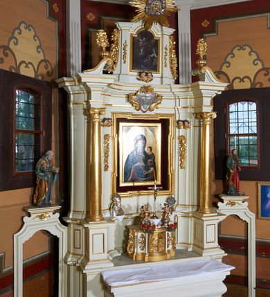 Zdjęcie nr 3: Ołtarz architektoniczny, drewniany, jednoosiowy, jednokondygnacyjny z bramkami. Mensa wąska, prostopadłościenna o ściankach wklęsło-wypukłych. Tabernakulum w kształcie prostopadłościennej skrzynki z przodu o linii wklęsło-wypukłej z uskokami. Ustawione jest na  wysokim cokole, flankowane parą szerokich, wklęsłych pilastrów, zdobionych ornamentem złożonym z przeplatających się wolut i kampanul. Ścianka frontowa wypukła, w polu prostokątne, metalowe drzwiczki, zdobione kiśćmi winogron i kłosami zbóż, pośrodku łaciński prosty krzyż. Całość zamknięta profilowanym gzymsem. Po bokach tabernakulum zwisy z kampanul, a na skrajach płaskorzeźbione uszy z liści akantu.  Do górnej krawędzi przybite gwoździem na trzech tulejach lampki oliwne. Nad tabernakulum tron wystawienia z rzeźbionymi w drewnie aniołkami na obłokach adorującymi krucyfiks. 

Retabulum ustawione na zdwojonym cokole, ujęte zwielokrotnionymi pilastrami toskańskimi i dwiema kolumnami kompozytowymi na wysokich cokołach, ustawionymi pod kątem i podtrzymującymi profilowane, przerwane belkowanie. Pilastry od strony wewnętrznej ołtarza są wklęsłe, ozdobione dwiema parami uskrzydlonych główek anielskich i zwisami z kwiatów; od zewnątrz pilastry mają trzony wypukłe.  W polu głównym wnęka, ujęta ramą w kształcie stojącego prostokąta o uszatych narożach. We wnęce na czerwonym tle umieszczony obraz Matki Boskiej Piekarskiej, na zasuwach obrazy „Koronacja Matki Boskiej” oraz „Św. Mikołaj”. Nad obrazem kartusz o kształcie zbliżonym do rombu z ornamentami rocaille'owymi wokół; w polu napis „ALTARE / PRIVILEGI/ATUM”. Na osi kolumn, na przyczółku ustawione są wazony z kwiatami. 

Zwieńczenie w kształcie stojącego prostokąta, flankowane parą pilastrów podtrzymujących przerwane belkowanie, zamknięte gzymsem w formie łuku odcinkowego. Na szczycie promienista gloria z otokiem chmur pośrodku z płaskorzeźbionym monogramem IHS. W polu głównym obraz przedstawiający Ekstazę św. Teresy w kształcie stojącego prostokąta, zamknięty łukiem nadwieszonym. Po bokach zwieńczenia uszy z liści akantu i kwiatów. Pod obrazem uskrzydlona para główek aniołków. 

Bramki w formie stojącego prostokąta, flankowane węgarami, zamknięte wolutowym łukiem z ustawionymi na szczycie na niskich cokołach rzeźbami świętych: po lewej św. Piotra, a po prawej św. Pawła.  Przejście zamknięte łukiem wklęsło-wypukłym z uskokami. Struktura polichromowana w kolorze jasnobeżowym, ornamentyka złocona, detale srebrzone.
