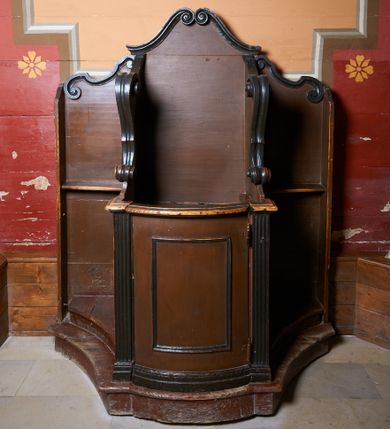 Zdjęcie nr 1: Usytuowany w nawie głównej, przy ścianie zachodniej pod chórem muzycznym. Konfesjonał o podstawie na planie zakończonym z jednej strony (od ściany) linią prostą, a z drugiej łukiem wklęsło-wypukłym z uskokiem. Drzwi zamykające wejście do siedziska księdza wypukłe, ujęte kanelowanymi lizenami, na profilowanej bazie. Pośrodku drzwi profilowana rama w kształcie stojącego prostokąta. Boczne, występujące ku górze ścianki ograniczające siedzisko zwieńczone fantazyjnymi łukami wklęsło-wypukłymi zakończonymi ślimacznicami. Ściana zaplecka zwieńczona dwiema stykającymi się wolutami. Boczne partie konfesjonału, po bokach siedziska księdza, ograniczone są od strony muru kościoła pionowymi ściankami i zakończonymi wolutami. U dołu tych partii konfesjonału stopnie-klęczniki. W ściankach flankujących z boków siedzisko księdza prześwity z grubą kratą, w kształcie stojącego prostokąta, zamkniętego łukiem nadwieszonym, ujęte w profilowaną ramę. 