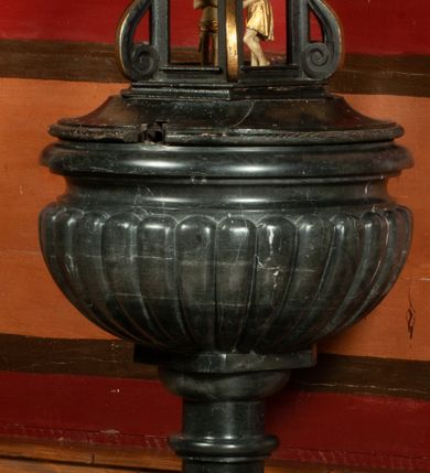 Zdjęcie nr 1: Chrzcielnica osadzona na wysokim, prostopadłościennym cokole, z trzonem w typie gruszkowym oraz czarą z puklami i profilowanym brzegiem. Pokrywa w kształcie ażurowej świątynki, na rzucie czworoboku, ujętej spływami wolutowymi, nakryta czworoboczną kopułką z krzyżem; wewnątrz św. Jana Chrzciciel chrzczący Jezusa w Jordanie. 

