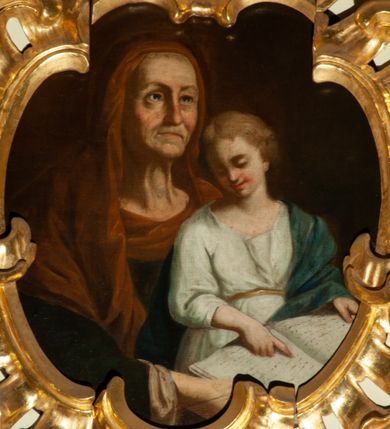 Zdjęcie nr 1: Obraz w kształcie zbliżonym do owalu, ujęty kartuszową, rocaille'ową ramą o nieregularnym, wewnętrznym obrysie ograniczającym pole obrazu. Na jednolitym ciemnym tle św. Anna, ukazana w półpostaci, z twarzą zwróconą w lewą stronę, trzymająca na kolanach młodzieńczą Marię, przedstawioną w trzech czwartych postaci. Święta Anna wyobrażona jako starsza kobieta o pokrytej zmarszczkami twarzy, ze wzrokiem wpatrzonym w dal. Jest ubrana w granatową suknię z długimi rękawami oraz brunatny welon założony na głowę i spływający na ramiona. Maria ubrana w białą sukienkę z podwiniętymi rękawami, przewiązaną w pasie złotym paskiem oraz w niebieski płaszcz założony na lewe ramię. Ma jasne włosy, średniej długości, przedzielone pośrodku przedziałkiem i młodzieńczą twarz. Maria w rękach trzyma otwartą księgę i prawą dłonią wskazuje na czytany tekst. Kolorystyka obrazu ciemna, najjaśniejszym akcentem jest szata Marii i księga.