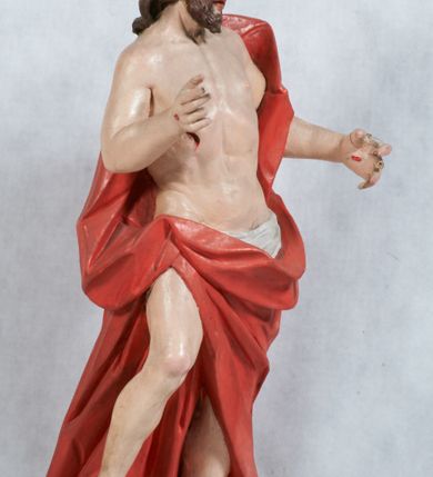 Zdjęcie nr 8: Rzeźba Chrystusa Zmartwychwstałego pełnoplastyczna, wolnostojąca, ustawiona na niskim cokole. Chrystus ukazany w całej postaci, ustawiony frontalnie, w delikatnym kontrapoście, ma prawą nogę ugiętą w kolanie i wspartą na czaszce z wężem. Ręce ma ugięte w łokciach i wyciągnięte przed siebie, w lewej trzyma chorągiew o długim drzewcu, a prawą unosi w geście błogosławieństwa. Jego twarz jest pociągła, o wysokim czole, długim i wąskim nosie, dużych oczach i rozchylonych ustach, okolona średniej długości, ciemną brodą i długimi, falowanymi włosami, które opadają na plecy i lewe ramię. Wokół głowy ma złoty nimb krzyżowy utworzony z wiązek promieni o nierównej długości. Chrystus ubrany jest w białe perizonium oraz czerwony płaszcz odsłaniający tors, otaczający figurę i przerzucony przez lewe ramię. Na dłoniach, stopach i boku zaznaczone są ślady męki. Polichromia ciała jest naturalistyczna, nimb pozłacany, drzewce chorągwi srebrzone.

