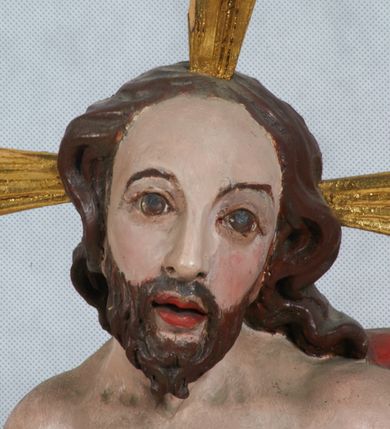 Zdjęcie nr 3: Rzeźba Chrystusa Zmartwychwstałego pełnoplastyczna, wolnostojąca, ustawiona na niskim cokole. Chrystus ukazany w całej postaci, ustawiony frontalnie, w delikatnym kontrapoście, ma prawą nogę ugiętą w kolanie i wspartą na czaszce z wężem. Ręce ma ugięte w łokciach i wyciągnięte przed siebie, w lewej trzyma chorągiew o długim drzewcu, a prawą unosi w geście błogosławieństwa. Jego twarz jest pociągła, o wysokim czole, długim i wąskim nosie, dużych oczach i rozchylonych ustach, okolona średniej długości, ciemną brodą i długimi, falowanymi włosami, które opadają na plecy i lewe ramię. Wokół głowy ma złoty nimb krzyżowy utworzony z wiązek promieni o nierównej długości. Chrystus ubrany jest w białe perizonium oraz czerwony płaszcz odsłaniający tors, otaczający figurę i przerzucony przez lewe ramię. Na dłoniach, stopach i boku zaznaczone są ślady męki. Polichromia ciała jest naturalistyczna, nimb pozłacany, drzewce chorągwi srebrzone.

