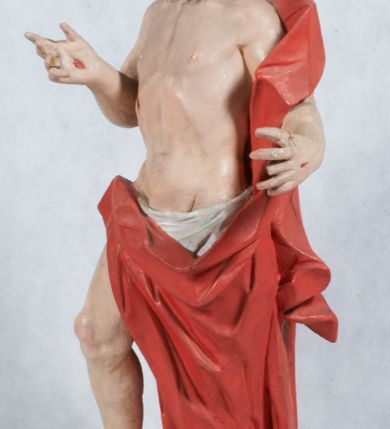 Zdjęcie nr 5: Rzeźba Chrystusa Zmartwychwstałego pełnoplastyczna, wolnostojąca, ustawiona na niskim cokole. Chrystus ukazany w całej postaci, ustawiony frontalnie, w delikatnym kontrapoście, ma prawą nogę ugiętą w kolanie i wspartą na czaszce z wężem. Ręce ma ugięte w łokciach i wyciągnięte przed siebie, w lewej trzyma chorągiew o długim drzewcu, a prawą unosi w geście błogosławieństwa. Jego twarz jest pociągła, o wysokim czole, długim i wąskim nosie, dużych oczach i rozchylonych ustach, okolona średniej długości, ciemną brodą i długimi, falowanymi włosami, które opadają na plecy i lewe ramię. Wokół głowy ma złoty nimb krzyżowy utworzony z wiązek promieni o nierównej długości. Chrystus ubrany jest w białe perizonium oraz czerwony płaszcz odsłaniający tors, otaczający figurę i przerzucony przez lewe ramię. Na dłoniach, stopach i boku zaznaczone są ślady męki. Polichromia ciała jest naturalistyczna, nimb pozłacany, drzewce chorągwi srebrzone.

