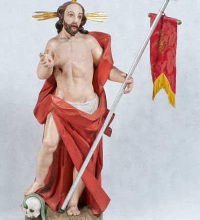 Zdjęcie nr 1: Rzeźba Chrystusa Zmartwychwstałego pełnoplastyczna, wolnostojąca, ustawiona na niskim cokole. Chrystus ukazany w całej postaci, ustawiony frontalnie, w delikatnym kontrapoście, ma prawą nogę ugiętą w kolanie i wspartą na czaszce z wężem. Ręce ma ugięte w łokciach i wyciągnięte przed siebie, w lewej trzyma chorągiew o długim drzewcu, a prawą unosi w geście błogosławieństwa. Jego twarz jest pociągła, o wysokim czole, długim i wąskim nosie, dużych oczach i rozchylonych ustach, okolona średniej długości, ciemną brodą i długimi, falowanymi włosami, które opadają na plecy i lewe ramię. Wokół głowy ma złoty nimb krzyżowy utworzony z wiązek promieni o nierównej długości. Chrystus ubrany jest w białe perizonium oraz czerwony płaszcz odsłaniający tors, otaczający figurę i przerzucony przez lewe ramię. Na dłoniach, stopach i boku zaznaczone są ślady męki. Polichromia ciała jest naturalistyczna, nimb pozłacany, drzewce chorągwi srebrzone.

