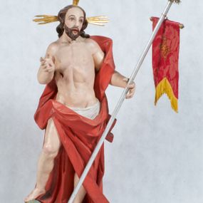 Zdjęcie nr 1: Rzeźba Chrystusa Zmartwychwstałego pełnoplastyczna, wolnostojąca, ustawiona na niskim cokole. Chrystus ukazany w całej postaci, ustawiony frontalnie, w delikatnym kontrapoście, ma prawą nogę ugiętą w kolanie i wspartą na czaszce z wężem. Ręce ma ugięte w łokciach i wyciągnięte przed siebie, w lewej trzyma chorągiew o długim drzewcu, a prawą unosi w geście błogosławieństwa. Jego twarz jest pociągła, o wysokim czole, długim i wąskim nosie, dużych oczach i rozchylonych ustach, okolona średniej długości, ciemną brodą i długimi, falowanymi włosami, które opadają na plecy i lewe ramię. Wokół głowy ma złoty nimb krzyżowy utworzony z wiązek promieni o nierównej długości. Chrystus ubrany jest w białe perizonium oraz czerwony płaszcz odsłaniający tors, otaczający figurę i przerzucony przez lewe ramię. Na dłoniach, stopach i boku zaznaczone są ślady męki. Polichromia ciała jest naturalistyczna, nimb pozłacany, drzewce chorągwi srebrzone.

