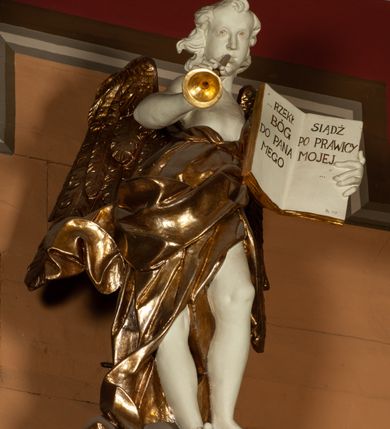 Zdjęcie nr 3: Rzeźba pełnoplastyczna, przedstawiająca anioła stojącego na obłoku z lewą nogą ugiętą w kolanie, który dmie w trąbę, a w lewej dłoni trzyma otwartą księgę z napisem „RZEKŁ / BÓG / DO PANA / MEGO / SIĄDŹ / PO PRAWICY / MOJEJ”. Twarz podłużna, okolona długimi, kręconymi włosami z wyraźnie zaznaczonym podbródkiem. Anioł owinięty jest bogato drapowaną tkaniną, tworzącą ostro załamujące się fałdy. Karnacja biała; szaty, skrzydła, trąbka i elementy księgi złocone.