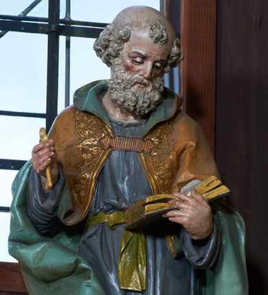 Zdjęcie nr 1: Rzeźba ustawiona na ośmiobocznej podstawie, wolnostojąca, pełnoplastyczna. Święty ukazany całej postaci, stojący, z głową skłonioną delikatnie w dół, w kierunku trzymanej w lewej dłoni otwartej księgi; w prawej trzyma złoty klucz. Twarz szeroka, o rysach starszego mężczyzny, okolona bujną, siwą, średniej długości brodą. Na głowie łysina oraz kępka włosów nad czołem. Święty ubrany w długą, fioletową suknię z długimi rękawami, przewiązaną złotym paskiem oraz brązowy płaszcz z zieloną podszewką, spięty na piersi, dekorowany na brzegach lamówką pokrytą roślinnym ornamentem; na nogach sandały. Polichromia w odsłoniętych partiach ciała naturalistyczna. 

