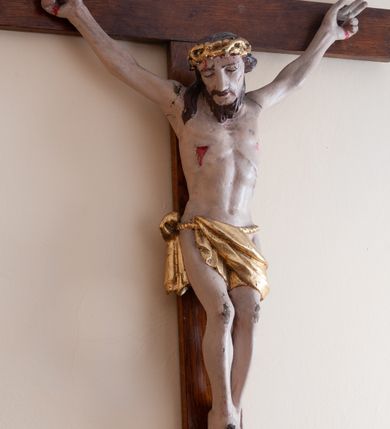 Zdjęcie nr 2: Rzeźba Chrystusa przybita do krzyża trzema gwoździami. Chrystus ukazany w typie Cristo morte, o delikatnie esowato wygiętej sylwetce, w lekkim zwisie, z głową nieznacznie pochyloną na prawą stronę. Chrystus ma masywne dłonie i stopy, wyraźnie podkreśloną linię żeber, sylwetkę szczupłą. Jego twarz jest podłużna, okolona krótką brodą, ciemnobrązowe włosy spływają na prawe ramię. Na głowie ma założoną koronę cierniową. Jego biodra oplata złocone perizonium zawieszone na sznurze. Z dłoni, stóp i boku Chrystusa spływają strużki krwi. Polichromia ciała naturalistyczna, detale korona cierniowa i perizonium złocone. Krzyż prosty, gładki, malowany w kolorze drewna. 
