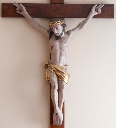 Zdjęcie nr 1: Rzeźba Chrystusa przybita do krzyża trzema gwoździami. Chrystus ukazany w typie Cristo morte, o delikatnie esowato wygiętej sylwetce, w lekkim zwisie, z głową nieznacznie pochyloną na prawą stronę. Chrystus ma masywne dłonie i stopy, wyraźnie podkreśloną linię żeber, sylwetkę szczupłą. Jego twarz jest podłużna, okolona krótką brodą, ciemnobrązowe włosy spływają na prawe ramię. Na głowie ma założoną koronę cierniową. Jego biodra oplata złocone perizonium zawieszone na sznurze. Z dłoni, stóp i boku Chrystusa spływają strużki krwi. Polichromia ciała naturalistyczna, detale korona cierniowa i perizonium złocone. Krzyż prosty, gładki, malowany w kolorze drewna. 
