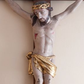 Zdjęcie nr 1: Rzeźba Chrystusa przybita do krzyża trzema gwoździami. Chrystus ukazany w typie Cristo morte, o delikatnie esowato wygiętej sylwetce, w lekkim zwisie, z głową nieznacznie pochyloną na prawą stronę. Chrystus ma masywne dłonie i stopy, wyraźnie podkreśloną linię żeber, sylwetkę szczupłą. Jego twarz jest podłużna, okolona krótką brodą, ciemnobrązowe włosy spływają na prawe ramię. Na głowie ma założoną koronę cierniową. Jego biodra oplata złocone perizonium zawieszone na sznurze. Z dłoni, stóp i boku Chrystusa spływają strużki krwi. Polichromia ciała naturalistyczna, detale korona cierniowa i perizonium złocone. Krzyż prosty, gładki, malowany w kolorze drewna. 
