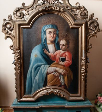 Zdjęcie nr 1: Feretron dwustronny z obrazami Matki Boskiej Śnieżnej oraz św. Mikołaja ustawiony na prostopadłościennym cokole, zaopatrzonym w otwory na drążki do noszenia. Cokół wsparty na dwóch postumentach na planie kwadratu. Obrazy w kształcie stojącego prostokąta, zamkniętego łukiem nadwieszonym w profilowanym ramach, zdobionych rzeźbionym ornamentem rocaille&#039;owym. W zwieńczeniu nad obrazem św. Mikołaja Oko Opatrzności na tle promienistej glorii, a nad obrazem Matki Boskiej cztery obłoki na tle glorii (symbol niezachowany). Struktura feretronu malowana na zielono, detale, ornamentyka i profilowania złocone. Matka Boska ukazana na obrazie w półpostaci, frontalnie, z Dzieciątkiem Jezus na lewej ręce. Ręce Marii skrzyżowane na tle postaci Dzieciątka. W lewej dłoni Matka Boska trzyma białą chustę. Twarz podłużna, z dużymi oczami i zarumienionymi policzkami. Maria ubrana jest w białą suknię z długimi rękawami, u szyi obwiedzioną złotą lamówką oraz błękitny maforion ze złotą gwiazdą na prawym ramieniu. Dzieciątko ukazane w pozycji siedzącej, zwrócone trzy czwarte w prawo, z prawą ręką uniesioną w geście błogosławieństwa, z księgą w lewej. Twarz Dzieciątka o pulchnych policzkach i wysokim czole; włosy jasne, kędzierzawe. Ubrane jest w czerwoną sukienkę z długimi rękawami oraz ugrową szatę przerzuconą przez kolana. Na głowach Marii i Dzieciątka korony w typie zamkniętym zwieńczone krzyżykiem zatkniętym na kuli. Tło w odcieniach ugru i brązu. Po drugiej stronie feretronu obraz św. Mikołaja. Święty ukazany w centrum kompozycji, do wysokości kolan. W lewym ręku trzyma księgę, na której ułożone są trzy złote kule, prawą rękę unosi do góry na wysokości piersi. Twarz podłużna, okolona długą i siwą brodą; włosy siwe i krótkie, częściowo z łysiną. Ubrany jest w białą albę, złoty ornat oraz omoforion. Tło w odcieniach ugru i brązu. 
