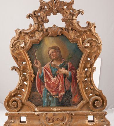 Zdjęcie nr 1: Feretron dwustronny z obrazami św. Małgorzaty oraz św. Barbary ustawiony na prostopadłościennym cokole, zaopatrzonym w otwory na drążki do noszenia, pośrodku zdobionym rocaille&#039;owym kartuszem z napisami, po jednej stronie „Św(ięta) / Małgorzata”, po drugiej „Św(ięta) Barbara”. Obrazy w kształcie stojących prostokątów o bokach wklęsło-wypukłych z uskokami. Ujęte bogato dekorowaną, rzeźbioną ramą, zdobioną ornamentem rocaille&#039;owym, w narożach uformowanym na kształt wolut. Święta Małgorzata ukazana w centrum kompozycji, w postawie stojącej, do wysokości trzech czwartych, z krzyżem w prawej dłoni i z palmą męczeństwa w lewej. Twarz owalna, z krótkim i wąskim nosem, mocno zarumienionymi policzkami; wzrokiem skierowanym do góry. Włosy długie, jasne, spływające na plecy. Dłonie smukłe, wysublimowane. Ubrana w niebieską suknię z długimi rękawami oraz czerwony płaszcz zarzucony na plecy. Na głowie brązowy welon spływający na prawe ramię; we włosy wpięte klejnoty. W dolnym, lewym narożu dzikie zwierzę, po prawej stronie ognisko. Po drugiej stronie feretronu obraz z wizerunkiem św. Barbary ukazanej w centrum kompozycji, w postawie stojącej, do wysokości trzech czwartych, z palmą męczeństwa w prawej dłoni i mieczem, skierowanym ostrzem w dół w lewej. Twarz owalna, z krótkim i wąskim nosem, rozchylone usta, mocno zarumienione policzki. Wzrok skierowany na znajdujący się po prawej stronie obrazu kielich z hostią. Włosy długie, spływające na plecy, częściowo schowane pod białym welonem. Dłonie smukłe, delikatne. Ubrana jest w niebieską suknię z długimi rękawami, przewiązaną paskiem i z dużym dekoltem oraz czerwony płaszcz zarzucony na plecy i lewe ramię. W górnym, lewym rogu obrazu wieża. Tło w kolorach ugru. Struktura feretronu złocona. 
