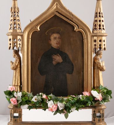 Zdjęcie nr 1: Feretron dwustronny z obrazami św. Stanisława Kostki oraz Anioła Stróża. Konstrukcja feretronu osadzona na dwóch nóżkach na planie koła, wspierających dwa wieloboczne w rzucie cokoły, połączone listwami stabilizującymi konstrukcję feretronu; cokoły zaopatrzone w otwory na drążki do noszenia. Na cokołach ustawione dwie rzeźby niezidentyfikowanych świętych, ujętych z profilu, nad nimi nadwieszone baldachimy zwieńczone stylizowanymi kwiatonami. W centrum tej konstrukcji obrazy ujęte w profilowaną ramę, zamkniętą łukiem ostrym o spłaszczonych ramionach, zwieńczoną krzyżykiem łacińskim o trójlistnie zakończonych ramionach. Struktura feretronu złocona. Na obrazie Anioł Stróż  ukazany jest po prawej stronie kompozycji, w postawie stojącej, widoczny z lewego profilu, pochylony nad dzieckiem bawiącym się na kwietnej łące. Ubrany jest w białą, długą sukienkę. Tło obrazu jednolite, ciemnoniebieskie. Po drugiej stronie feretronu znajduje się wizerunek św. Stanisława Kostki. Święty ukazany do kolan, stojący frontalnie, delikatnie zwrócony w lewo, z rękami złożonymi na piersi, z różańcem w dłoniach. Twarz szeroka, ze wzrokiem skierowanym ku górze, włosy krótkie i jasnobrązowe. Święty ubrany jest w sutannę jezuicką. Wokół głowy ma złoty, okrągły nimb. Tło obrazu jednolite, brązowe.
