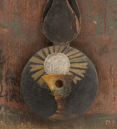 Zdjęcie nr 6: Zegar w kształcie stojącego prostokąta. W części centralnej okrągła tarcza z pejzażem oraz kołem pośrodku, ozdobionym kielichem z hostią, od którego odchodzą dwie fantazyjnie wycięte wskazówki. Wokół tarczy z pejzażem dwa okręgi, w pierwszym liczby od 1 do 31, w drugim, zewnętrznym – łacińskie nazwy miesięcy. W górnej części kompozycji biała banderola z napisem: „Renovatio Sanctissimi Sacramenti”. Poniżej, wpisany w koło na czerwonym tle monogram Chrystusa. Tło czarne.

