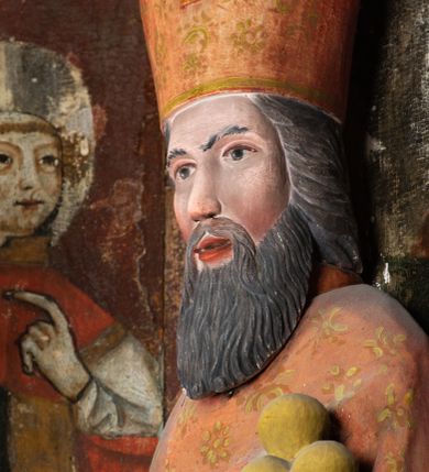 Zdjęcie nr 10: Rzeźba pełnoplastyczna, przyścienna, ścięta z tyłu; całopostaciowe przedstawienie stojącego na niewysokim postumencie św. Mikołaja. Święty ukazany frontalnie. Twarz pociągła, o wyrazistych rysach i długim, brązowym zaroście, włosy sięgające szyi. Święty w stroju pontyfikalnym: ubrany w długą, białą albę oraz jasnoczerwoną dalmatykę lub tunicelę i ornat sięgający do połowy łydek. Na głowie infuła biskupia. W lewej ręce prostopadłościenna skrzyneczka z napisem: IHS i trzema złotymi kulami, w prawej pastorał. Figura umieszczona w prostopadłościennej szafie oltarzowej o skośnych ścianach bocznych zdobionych figuralną polichromią. Po lewej stronie św. Wawrzyniec, po prawej św. Szczepan, na wysokości głowy świętego polichromowana, jasna aureola.