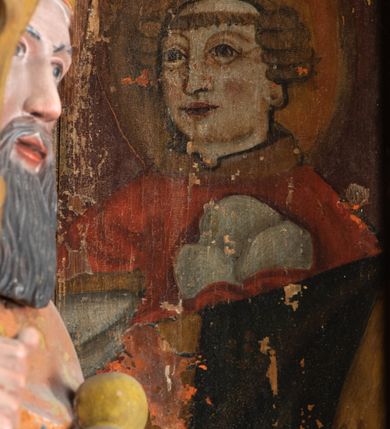 Zdjęcie nr 9: Rzeźba pełnoplastyczna, przyścienna, ścięta z tyłu; całopostaciowe przedstawienie stojącego na niewysokim postumencie św. Mikołaja. Święty ukazany frontalnie. Twarz pociągła, o wyrazistych rysach i długim, brązowym zaroście, włosy sięgające szyi. Święty w stroju pontyfikalnym: ubrany w długą, białą albę oraz jasnoczerwoną dalmatykę lub tunicelę i ornat sięgający do połowy łydek. Na głowie infuła biskupia. W lewej ręce prostopadłościenna skrzyneczka z napisem: IHS i trzema złotymi kulami, w prawej pastorał. Figura umieszczona w prostopadłościennej szafie oltarzowej o skośnych ścianach bocznych zdobionych figuralną polichromią. Po lewej stronie św. Wawrzyniec, po prawej św. Szczepan, na wysokości głowy świętego polichromowana, jasna aureola.