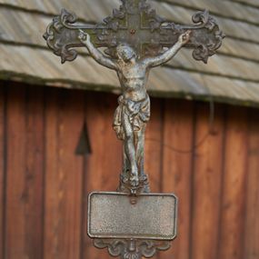 Zdjęcie nr 1: Żeliwny krucyfiks na kamiennym, graniastosłupowym postumencie zakończonym półkuliście. Metalowa, półplastyczna figura Ukrzyżowanego ubranego w krótkie perizonium związane po lewej stronie. Ramiona tworzą kształt litery U; głowa przechylona w prawo. Nogi przebite jednym gwoździem. Zakończenia i przecięcie ramion krzyża zdobione motywami roślinnymi. W górnej części belki pionowej titulus z literami: I.N.R.I.;  poniżej stóp Chrystusa tabliczka w kształcie leżącego prostokąta, z  wolutowo - roślinnym podwieszeniem (fartuchem). Podstawa krzyża w formie symetrycznego ornamentu roślinnego z dwoma dużymi kwiatami, na których stoi para aniołków ustawionych antytetycznie, ubranych w krótkie tuniki, ze złożonymi rękami.