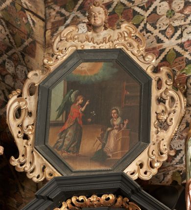 Zdjęcie nr 5: Obraz w kształcie stojącego ośmioboku z przedstawieniem Zwiastowania NMP, we wnętrzu z oknem w tle. W prawej dolnej części obrazu klęcząca na klęczniku Maria w ujęciu trzy czwarte, zwracająca głowę w stronę unoszącego się tuż nad posadzką Archanioła Gabriela. Archanioł znajduje się w lewej części obrazu, ukazany z profilu, zwraca się w stronę Marii, prawą rękę unosi do góry, w lewej trzyma białą lilię. Scena ukazana we wnętrzu. W górnej partii obrazu świetlisty obłok z gołębicą Ducha Świętego. Kolorystyka utrzymana w tonacji ciepłej, z przewagą brązów, ugrów, bieli, żółcieni i czerwieni.