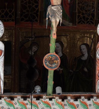 Zdjęcie nr 4: Pośrodku belki tęczowej krzyż widlasty z figurą martwego Chrystusa Ukrzyżowanego, flankowany przez malowane na desce postacie Matki Boskiej i św. Jana Ewangelisty. Obrazy w kształcie wyciętego w desce konturu postaci. Krzyż w formie drzewa życia, z pojedynczymi wypustkami, na zakończeniach ramion medaliony z przedstawieniami symboli Ewangelistów z banderolami, górny medalion pusty; pod nim ukośny titulus w formie banderoli z napisem: INRI. Figura Chrystusa w lekkim zwisie, o szeroko rozłożonych ramionach, głowa opadająca; nogi silnie zgięte w kolanach, podkulone; stopy przebite jednym gwoździem, założone prawa na lewą. Ciało o niewłaściwych proporcjach anatomicznych, z silnie podkreśloną klatką piersiową oraz zaznaczonymi śladami męki. Twarz pociągła, o delikatnie rzeźbionych rysach, okolona zarostem. Włosy długie, falowane, opadają na plecy, na głowie korona cierniowa. Perizonium długie, sięgające kolan, ściśle opina biodra, z dwoma zwisami tkaniny po bokach. Polichromia naturalistyczna.