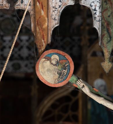 Zdjęcie nr 6: Pośrodku belki tęczowej krzyż widlasty z figurą martwego Chrystusa Ukrzyżowanego, flankowany przez malowane na desce postacie Matki Boskiej i św. Jana Ewangelisty. Obrazy w kształcie wyciętego w desce konturu postaci. Krzyż w formie drzewa życia, z pojedynczymi wypustkami, na zakończeniach ramion medaliony z przedstawieniami symboli Ewangelistów z banderolami, górny medalion pusty; pod nim ukośny titulus w formie banderoli z napisem: INRI. Figura Chrystusa w lekkim zwisie, o szeroko rozłożonych ramionach, głowa opadająca; nogi silnie zgięte w kolanach, podkulone; stopy przebite jednym gwoździem, założone prawa na lewą. Ciało o niewłaściwych proporcjach anatomicznych, z silnie podkreśloną klatką piersiową oraz zaznaczonymi śladami męki. Twarz pociągła, o delikatnie rzeźbionych rysach, okolona zarostem. Włosy długie, falowane, opadają na plecy, na głowie korona cierniowa. Perizonium długie, sięgające kolan, ściśle opina biodra, z dwoma zwisami tkaniny po bokach. Polichromia naturalistyczna.