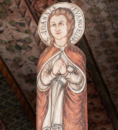 Zdjęcie nr 1: W centrum krzyż widlasty z figurą martwego Chrystusa Ukrzyżowanego; flankowany przez malowane na desce postacie Matki Boskiej i św. Jana. Obrazy w kształcie wyciętego obrysu postaci. Obraz z Matką Boską po prawej stronie krzyża. Maria zwrócona en face, z rękoma skrzyżowanymi na piersi i głową skierowaną w stronę krzyża. Twarz owalna,, o młodzieńczych rysach. Ubrana w czerwoną suknię z długimi, wąskimi rękawami ze złotą lamówką oraz biały płaszcz narzucony na głowę i ramiona, opadający falami po bokach. Wokół głowy nimb z napisem: S. MARIA ORA PRO NOBIS PECCATOR[IBUS] Obraz z przedstawieniem św. Jana po lewej stronie krzyża. Święty zwrócony en face, z dłońmi złożonymi na piersi, lewą podtrzymuje zamkniętą księgę. Twarz owalna, o pełnych policzkach i wyraźnych, młodzieńczych rysach. Włosy długie poskręcane w pukle i opadające na ramiona. Ubrany w białą tunikę o wąskich długich rękawach, drapowaną w równoległe fałdy oraz czerwony płaszcz zapięty przy szyi fibulą, opadający kaskadami na ramiona i boki. Wokół głowy nimb z napisem: S. IOANNES EVANGELISTA. Malowane płaską plamą barwną z silnym konturem.