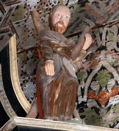 Zdjęcie nr 1: Rzeźba pełnoplastyczna, drążona, ustawiona na prostopadłościennym cokole. Święty ukazany frontalnie, w wykroku, przechylony do tyłu, opierając się o stojący na nim krzyż w kształcie litery X; lewą ręką podtrzymuje belkę, prawa pozostaje opuszczona wzdłuż ciała. Święty ubrany w złotą, drapowaną tunikę z długim rękawem oraz srebrny płaszcz przerzucony przez pierś i zawinięty na biodrze.