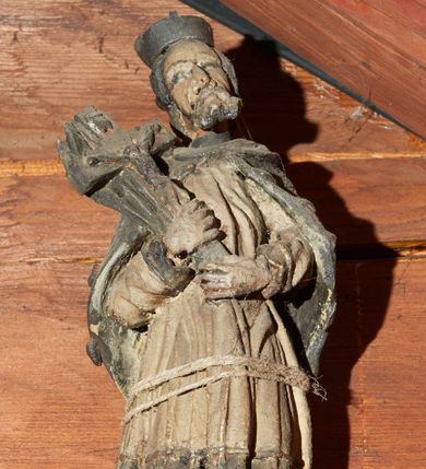 Zdjęcie nr 1: Rzeźba pełnoplastyczna, ustawiona na niewysokim cokole na rzucie prostokąta. Święty ukazany frontalnie, w kontrapoście, o esowato wygiętej sylwetce, z głową przechyloną na prawe ramię. Ręce ugięte w łokciach. Obiema dłońmi podtrzymuje przed sobą krucyfiks oparty na prawym ramieniu. Twarz pociągła, okolona zarostem; włosy krótkie. Ubrany w czarną sutannę, białą delikatnie drapowaną komżę, na ramionach mucet. Na głowie biret. Polichromia naturalistyczna.
