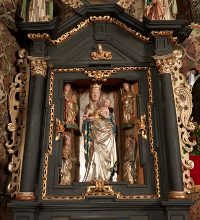 Zdjęcie nr 1: Nastawa ołtarzowa architektoniczna, jednoosiowa, jednokondygnacyjna, z wydzieloną predellą i zwieńczeniem, na cokole. Ołtarz kamienny z narzutem z tynku, sarkofagowy, wklęsło-wypukły. Mensa drewniana z portatylem z marmuru dębnickiego.Predella dekorowana płyciną w formie wydłużonego prostokąta z uszakami z malowanym przedstawieniem Bożego Narodzenia. Nastawa ujęta parą kolumn o kapitelach korynckich podtrzymujących pełne belkowanie belkowanie i gzyms, w części środkowej wyłamane ku górze trójbocznie. W polu środkowym nisza w formie stojącego prostokąta z uszakami, ujęta prostą ramą, wewnątrz gotycka szafa z figurą Matki Boskiej z Dzieciątkiem i czterech świętych dziewic. Na belkowaniu, w osi podpór figury św. Stanisława i św. Marcina (?). W zwieńczeniu ośmioboczny obraz z przedstawieniem Zwiastowania, w prostej ramie oraz bogatym obramieniu z ażurowych motywów ornamentu małżowinowo-chrząstkowego; u szczytu główka aniołka ze skrzydłami. Nastawa flankowana uszami utworzonymi z motywów ornamentu małżowinowo-chrząstkowego. W polu ponad niszą z obrazem rzeźbiona półpostać Boga Ojca. Gzyms u spodu dekorowany ornamentem małżowinowo-chrząstkowym. Struktura polichromowana na czarno, kapitele kolumn i część ornamentów srebrzone, pozostałe motywy ornamentalne złocone.