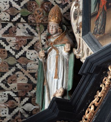 Zdjęcie nr 49: Nastawa ołtarzowa architektoniczna, jednoosiowa, jednokondygnacyjna, z wydzieloną predellą i zwieńczeniem, na cokole. Ołtarz kamienny z narzutem z tynku, sarkofagowy, wklęsło-wypukły. Mensa drewniana z portatylem z marmuru dębnickiego.Predella dekorowana płyciną w formie wydłużonego prostokąta z uszakami z malowanym przedstawieniem Bożego Narodzenia. Nastawa ujęta parą kolumn o kapitelach korynckich podtrzymujących pełne belkowanie belkowanie i gzyms, w części środkowej wyłamane ku górze trójbocznie. W polu środkowym nisza w formie stojącego prostokąta z uszakami, ujęta prostą ramą, wewnątrz gotycka szafa z figurą Matki Boskiej z Dzieciątkiem i czterech świętych dziewic. Na belkowaniu, w osi podpór figury św. Stanisława i św. Marcina (?). W zwieńczeniu ośmioboczny obraz z przedstawieniem Zwiastowania, w prostej ramie oraz bogatym obramieniu z ażurowych motywów ornamentu małżowinowo-chrząstkowego; u szczytu główka aniołka ze skrzydłami. Nastawa flankowana uszami utworzonymi z motywów ornamentu małżowinowo-chrząstkowego. W polu ponad niszą z obrazem rzeźbiona półpostać Boga Ojca. Gzyms u spodu dekorowany ornamentem małżowinowo-chrząstkowym. Struktura polichromowana na czarno, kapitele kolumn i część ornamentów srebrzone, pozostałe motywy ornamentalne złocone.