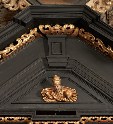 Zdjęcie nr 43: Retabulum ołtarzowe z dużą rzeźbą Matki Boskiej z Dzieciątkiem oraz mniejszymi o połowę czterema rzeźbami Świętych Dziewic umieszczonymi w prostopadłościennej szafie na rzucie trapezu (z ukośnie ustawionymi ściankami bocznymi). Rzeźby pełnoplastyczne, ścięte z tyłu, drążone, ustawione na cokolikach. Pośrodku figura Matki Boskiej w stylu gotyku międzynarodowego; zwrócona en face, w delikatnym kontrapoście, o esowato wygiętej sylwetce, podtrzymuje na obu rękach wpółleżące Dzieciatko. Twarz owalna z podwójnym podbródkiem, rysy twarzy płytko rzeźbione, delikatne, długi, prosty nos. Włosy upięte z tyłu. Maria ubrana w srebrzoną suknię z tkaniną drapowaną po środku w trzy fałdy misowe oraz złocony płaszcz podbity na niebieską podszewką, spływający od tyłu głowy na ramiona i boki, w układzie kaskadowym. Na głowie korona otwarta. Dzieciatko wpółleżące, zwrócone en trois quarts w prawo, prawą ręka ujmuje Matkę za szyję, w lewej trzyma złotą kulę. Twarz okrągła, duże uszy, włosy krótkie, kręcone. W partii bioder przepasany ściśle przylegającą, złotą tkaniną, delikatnie drapowaną. Na lewej ściance szafy u góry figurka św. Cecylii, zwróconej en face, o esowato wygiętej sylwetce, w lewej ręce, opartej na biodrze trzyma piszczałki, prawa wyciągnięta do przodu. Twarz okrągła o pełnych policzkach i płytko rzeźbionych rysach twarzy, włosy długie, falujące fakturowane, spływające przez ramiona na plecy. Ubrana w srebrzoną suknię oraz złocony płaszcz z czerwoną podszewką, spięty na piersi fibulą, z obfitą draperią przewieszoną przez ramiona, opadająca na froncie fałdami misowymi oraz spływającymi kaskadami od ramion. Na głowie blok drewna z namalowaną koroną otwartą.Na lewej ściance u dołu figura św. Katarzyny Aleksandryjskiej, zwróconej en face, w prawej ręce podtrzymuje koło, lewą wyciąga do przodu. Twarz okrągła, policzki pełne, o wysokim czole, nos duży, oczy duże delikatnie zarysowane. Włosy falowane, fakturowane, spływają na plecy. Święta ubrana w srebrzona suknię przepasaną w talii oraz złocony płaszcz spięty broszą na piersi, z obfitą draperią przewieszoną przez ramiona, opadająca na froncie misowymi fałdami i spływającymi kaskadami od ramion. Na głowie blok drewna z namalowaną koroną otwartą. Na prawej ściance u góry figura św. Doroty, zwrócona en face w delikatnym kontrapoście, prawa ręką podtrzymuje koszyk, lewą wskazuje na niego. Twarz owalna, pełna, delikatne rysy, wąski zadarty nos. Włosy falowane, fakturowane, opadają na tył głowy. Ubrana w złotą suknię, delikatnie drapowaną u dołu, oraz srebrzony płaszcz podbity czerwoną podszewką, spięty na piersi i układający się z przodu w fałdy misowe. Na głowie blok drewna z namalowaną koroną otwartą. Na prawej ściance u dołu figura św. Barbary, zwróconej en face, o esowato przegiętej sylwetce, obiema rękami przytrzymuje opartą na lewym ramieniu wieżę. Twarz owalna, pełna, delikatne rysy, wąski zadarty nos. Włosy falowane, fakturowane, opadają na tył głowy. Ubrana w suknię i srebrzony płaszcz z niebieską podszewką, spięty na piersi fibulą, przerzucony przez ramiona z obfitą partią materiału układającą się z przodu w fałdy misowe. Na głowie blok drewna z namalowaną koroną otwartą. Karnacje w tonacji naturalnej, szaty srebrzone i złocone.