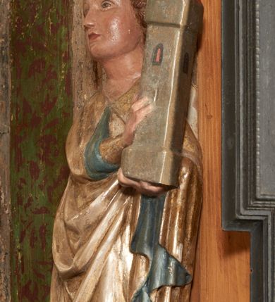 Zdjęcie nr 32: Retabulum ołtarzowe z dużą rzeźbą Matki Boskiej z Dzieciątkiem oraz mniejszymi o połowę czterema rzeźbami Świętych Dziewic umieszczonymi w prostopadłościennej szafie na rzucie trapezu (z ukośnie ustawionymi ściankami bocznymi). Rzeźby pełnoplastyczne, ścięte z tyłu, drążone, ustawione na cokolikach. Pośrodku figura Matki Boskiej w stylu gotyku międzynarodowego; zwrócona en face, w delikatnym kontrapoście, o esowato wygiętej sylwetce, podtrzymuje na obu rękach wpółleżące Dzieciatko. Twarz owalna z podwójnym podbródkiem, rysy twarzy płytko rzeźbione, delikatne, długi, prosty nos. Włosy upięte z tyłu. Maria ubrana w srebrzoną suknię z tkaniną drapowaną po środku w trzy fałdy misowe oraz złocony płaszcz podbity na niebieską podszewką, spływający od tyłu głowy na ramiona i boki, w układzie kaskadowym. Na głowie korona otwarta. Dzieciatko wpółleżące, zwrócone en trois quarts w prawo, prawą ręka ujmuje Matkę za szyję, w lewej trzyma złotą kulę. Twarz okrągła, duże uszy, włosy krótkie, kręcone. W partii bioder przepasany ściśle przylegającą, złotą tkaniną, delikatnie drapowaną. Na lewej ściance szafy u góry figurka św. Cecylii, zwróconej en face, o esowato wygiętej sylwetce, w lewej ręce, opartej na biodrze trzyma piszczałki, prawa wyciągnięta do przodu. Twarz okrągła o pełnych policzkach i płytko rzeźbionych rysach twarzy, włosy długie, falujące fakturowane, spływające przez ramiona na plecy. Ubrana w srebrzoną suknię oraz złocony płaszcz z czerwoną podszewką, spięty na piersi fibulą, z obfitą draperią przewieszoną przez ramiona, opadająca na froncie fałdami misowymi oraz spływającymi kaskadami od ramion. Na głowie blok drewna z namalowaną koroną otwartą.Na lewej ściance u dołu figura św. Katarzyny Aleksandryjskiej, zwróconej en face, w prawej ręce podtrzymuje koło, lewą wyciąga do przodu. Twarz okrągła, policzki pełne, o wysokim czole, nos duży, oczy duże delikatnie zarysowane. Włosy falowane, fakturowane, spływają na plecy. Święta ubrana w srebrzona suknię przepasaną w talii oraz złocony płaszcz spięty broszą na piersi, z obfitą draperią przewieszoną przez ramiona, opadająca na froncie misowymi fałdami i spływającymi kaskadami od ramion. Na głowie blok drewna z namalowaną koroną otwartą. Na prawej ściance u góry figura św. Doroty, zwrócona en face w delikatnym kontrapoście, prawa ręką podtrzymuje koszyk, lewą wskazuje na niego. Twarz owalna, pełna, delikatne rysy, wąski zadarty nos. Włosy falowane, fakturowane, opadają na tył głowy. Ubrana w złotą suknię, delikatnie drapowaną u dołu, oraz srebrzony płaszcz podbity czerwoną podszewką, spięty na piersi i układający się z przodu w fałdy misowe. Na głowie blok drewna z namalowaną koroną otwartą. Na prawej ściance u dołu figura św. Barbary, zwróconej en face, o esowato przegiętej sylwetce, obiema rękami przytrzymuje opartą na lewym ramieniu wieżę. Twarz owalna, pełna, delikatne rysy, wąski zadarty nos. Włosy falowane, fakturowane, opadają na tył głowy. Ubrana w suknię i srebrzony płaszcz z niebieską podszewką, spięty na piersi fibulą, przerzucony przez ramiona z obfitą partią materiału układającą się z przodu w fałdy misowe. Na głowie blok drewna z namalowaną koroną otwartą. Karnacje w tonacji naturalnej, szaty srebrzone i złocone.