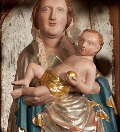 Zdjęcie nr 11: Retabulum ołtarzowe z dużą rzeźbą Matki Boskiej z Dzieciątkiem oraz mniejszymi o połowę czterema rzeźbami Świętych Dziewic umieszczonymi w prostopadłościennej szafie na rzucie trapezu (z ukośnie ustawionymi ściankami bocznymi). Rzeźby pełnoplastyczne, ścięte z tyłu, drążone, ustawione na cokolikach. Pośrodku figura Matki Boskiej w stylu gotyku międzynarodowego; zwrócona en face, w delikatnym kontrapoście, o esowato wygiętej sylwetce, podtrzymuje na obu rękach wpółleżące Dzieciatko. Twarz owalna z podwójnym podbródkiem, rysy twarzy płytko rzeźbione, delikatne, długi, prosty nos. Włosy upięte z tyłu. Maria ubrana w srebrzoną suknię z tkaniną drapowaną po środku w trzy fałdy misowe oraz złocony płaszcz podbity na niebieską podszewką, spływający od tyłu głowy na ramiona i boki, w układzie kaskadowym. Na głowie korona otwarta. Dzieciatko wpółleżące, zwrócone en trois quarts w prawo, prawą ręka ujmuje Matkę za szyję, w lewej trzyma złotą kulę. Twarz okrągła, duże uszy, włosy krótkie, kręcone. W partii bioder przepasany ściśle przylegającą, złotą tkaniną, delikatnie drapowaną. Na lewej ściance szafy u góry figurka św. Cecylii, zwróconej en face, o esowato wygiętej sylwetce, w lewej ręce, opartej na biodrze trzyma piszczałki, prawa wyciągnięta do przodu. Twarz okrągła o pełnych policzkach i płytko rzeźbionych rysach twarzy, włosy długie, falujące fakturowane, spływające przez ramiona na plecy. Ubrana w srebrzoną suknię oraz złocony płaszcz z czerwoną podszewką, spięty na piersi fibulą, z obfitą draperią przewieszoną przez ramiona, opadająca na froncie fałdami misowymi oraz spływającymi kaskadami od ramion. Na głowie blok drewna z namalowaną koroną otwartą.Na lewej ściance u dołu figura św. Katarzyny Aleksandryjskiej, zwróconej en face, w prawej ręce podtrzymuje koło, lewą wyciąga do przodu. Twarz okrągła, policzki pełne, o wysokim czole, nos duży, oczy duże delikatnie zarysowane. Włosy falowane, fakturowane, spływają na plecy. Święta ubrana w srebrzona suknię przepasaną w talii oraz złocony płaszcz spięty broszą na piersi, z obfitą draperią przewieszoną przez ramiona, opadająca na froncie misowymi fałdami i spływającymi kaskadami od ramion. Na głowie blok drewna z namalowaną koroną otwartą. Na prawej ściance u góry figura św. Doroty, zwrócona en face w delikatnym kontrapoście, prawa ręką podtrzymuje koszyk, lewą wskazuje na niego. Twarz owalna, pełna, delikatne rysy, wąski zadarty nos. Włosy falowane, fakturowane, opadają na tył głowy. Ubrana w złotą suknię, delikatnie drapowaną u dołu, oraz srebrzony płaszcz podbity czerwoną podszewką, spięty na piersi i układający się z przodu w fałdy misowe. Na głowie blok drewna z namalowaną koroną otwartą. Na prawej ściance u dołu figura św. Barbary, zwróconej en face, o esowato przegiętej sylwetce, obiema rękami przytrzymuje opartą na lewym ramieniu wieżę. Twarz owalna, pełna, delikatne rysy, wąski zadarty nos. Włosy falowane, fakturowane, opadają na tył głowy. Ubrana w suknię i srebrzony płaszcz z niebieską podszewką, spięty na piersi fibulą, przerzucony przez ramiona z obfitą partią materiału układającą się z przodu w fałdy misowe. Na głowie blok drewna z namalowaną koroną otwartą. Karnacje w tonacji naturalnej, szaty srebrzone i złocone.