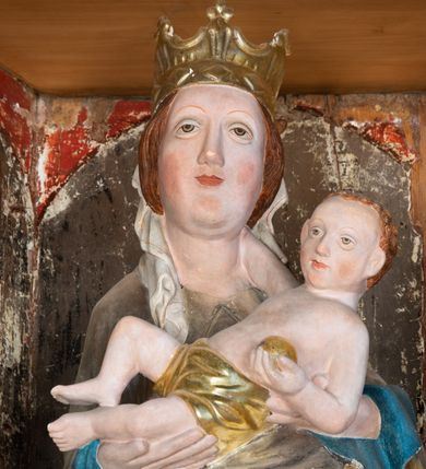 Zdjęcie nr 8: Retabulum ołtarzowe z dużą rzeźbą Matki Boskiej z Dzieciątkiem oraz mniejszymi o połowę czterema rzeźbami Świętych Dziewic umieszczonymi w prostopadłościennej szafie na rzucie trapezu (z ukośnie ustawionymi ściankami bocznymi). Rzeźby pełnoplastyczne, ścięte z tyłu, drążone, ustawione na cokolikach. Pośrodku figura Matki Boskiej w stylu gotyku międzynarodowego; zwrócona en face, w delikatnym kontrapoście, o esowato wygiętej sylwetce, podtrzymuje na obu rękach wpółleżące Dzieciatko. Twarz owalna z podwójnym podbródkiem, rysy twarzy płytko rzeźbione, delikatne, długi, prosty nos. Włosy upięte z tyłu. Maria ubrana w srebrzoną suknię z tkaniną drapowaną po środku w trzy fałdy misowe oraz złocony płaszcz podbity na niebieską podszewką, spływający od tyłu głowy na ramiona i boki, w układzie kaskadowym. Na głowie korona otwarta. Dzieciatko wpółleżące, zwrócone en trois quarts w prawo, prawą ręka ujmuje Matkę za szyję, w lewej trzyma złotą kulę. Twarz okrągła, duże uszy, włosy krótkie, kręcone. W partii bioder przepasany ściśle przylegającą, złotą tkaniną, delikatnie drapowaną. Na lewej ściance szafy u góry figurka św. Cecylii, zwróconej en face, o esowato wygiętej sylwetce, w lewej ręce, opartej na biodrze trzyma piszczałki, prawa wyciągnięta do przodu. Twarz okrągła o pełnych policzkach i płytko rzeźbionych rysach twarzy, włosy długie, falujące fakturowane, spływające przez ramiona na plecy. Ubrana w srebrzoną suknię oraz złocony płaszcz z czerwoną podszewką, spięty na piersi fibulą, z obfitą draperią przewieszoną przez ramiona, opadająca na froncie fałdami misowymi oraz spływającymi kaskadami od ramion. Na głowie blok drewna z namalowaną koroną otwartą.Na lewej ściance u dołu figura św. Katarzyny Aleksandryjskiej, zwróconej en face, w prawej ręce podtrzymuje koło, lewą wyciąga do przodu. Twarz okrągła, policzki pełne, o wysokim czole, nos duży, oczy duże delikatnie zarysowane. Włosy falowane, fakturowane, spływają na plecy. Święta ubrana w srebrzona suknię przepasaną w talii oraz złocony płaszcz spięty broszą na piersi, z obfitą draperią przewieszoną przez ramiona, opadająca na froncie misowymi fałdami i spływającymi kaskadami od ramion. Na głowie blok drewna z namalowaną koroną otwartą. Na prawej ściance u góry figura św. Doroty, zwrócona en face w delikatnym kontrapoście, prawa ręką podtrzymuje koszyk, lewą wskazuje na niego. Twarz owalna, pełna, delikatne rysy, wąski zadarty nos. Włosy falowane, fakturowane, opadają na tył głowy. Ubrana w złotą suknię, delikatnie drapowaną u dołu, oraz srebrzony płaszcz podbity czerwoną podszewką, spięty na piersi i układający się z przodu w fałdy misowe. Na głowie blok drewna z namalowaną koroną otwartą. Na prawej ściance u dołu figura św. Barbary, zwróconej en face, o esowato przegiętej sylwetce, obiema rękami przytrzymuje opartą na lewym ramieniu wieżę. Twarz owalna, pełna, delikatne rysy, wąski zadarty nos. Włosy falowane, fakturowane, opadają na tył głowy. Ubrana w suknię i srebrzony płaszcz z niebieską podszewką, spięty na piersi fibulą, przerzucony przez ramiona z obfitą partią materiału układającą się z przodu w fałdy misowe. Na głowie blok drewna z namalowaną koroną otwartą. Karnacje w tonacji naturalnej, szaty srebrzone i złocone.