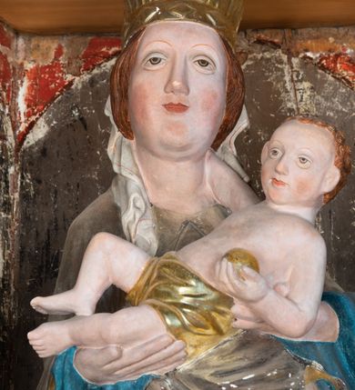 Zdjęcie nr 7: Retabulum ołtarzowe z dużą rzeźbą Matki Boskiej z Dzieciątkiem oraz mniejszymi o połowę czterema rzeźbami Świętych Dziewic umieszczonymi w prostopadłościennej szafie na rzucie trapezu (z ukośnie ustawionymi ściankami bocznymi). Rzeźby pełnoplastyczne, ścięte z tyłu, drążone, ustawione na cokolikach. Pośrodku figura Matki Boskiej w stylu gotyku międzynarodowego; zwrócona en face, w delikatnym kontrapoście, o esowato wygiętej sylwetce, podtrzymuje na obu rękach wpółleżące Dzieciatko. Twarz owalna z podwójnym podbródkiem, rysy twarzy płytko rzeźbione, delikatne, długi, prosty nos. Włosy upięte z tyłu. Maria ubrana w srebrzoną suknię z tkaniną drapowaną po środku w trzy fałdy misowe oraz złocony płaszcz podbity na niebieską podszewką, spływający od tyłu głowy na ramiona i boki, w układzie kaskadowym. Na głowie korona otwarta. Dzieciatko wpółleżące, zwrócone en trois quarts w prawo, prawą ręka ujmuje Matkę za szyję, w lewej trzyma złotą kulę. Twarz okrągła, duże uszy, włosy krótkie, kręcone. W partii bioder przepasany ściśle przylegającą, złotą tkaniną, delikatnie drapowaną. Na lewej ściance szafy u góry figurka św. Cecylii, zwróconej en face, o esowato wygiętej sylwetce, w lewej ręce, opartej na biodrze trzyma piszczałki, prawa wyciągnięta do przodu. Twarz okrągła o pełnych policzkach i płytko rzeźbionych rysach twarzy, włosy długie, falujące fakturowane, spływające przez ramiona na plecy. Ubrana w srebrzoną suknię oraz złocony płaszcz z czerwoną podszewką, spięty na piersi fibulą, z obfitą draperią przewieszoną przez ramiona, opadająca na froncie fałdami misowymi oraz spływającymi kaskadami od ramion. Na głowie blok drewna z namalowaną koroną otwartą.Na lewej ściance u dołu figura św. Katarzyny Aleksandryjskiej, zwróconej en face, w prawej ręce podtrzymuje koło, lewą wyciąga do przodu. Twarz okrągła, policzki pełne, o wysokim czole, nos duży, oczy duże delikatnie zarysowane. Włosy falowane, fakturowane, spływają na plecy. Święta ubrana w srebrzona suknię przepasaną w talii oraz złocony płaszcz spięty broszą na piersi, z obfitą draperią przewieszoną przez ramiona, opadająca na froncie misowymi fałdami i spływającymi kaskadami od ramion. Na głowie blok drewna z namalowaną koroną otwartą. Na prawej ściance u góry figura św. Doroty, zwrócona en face w delikatnym kontrapoście, prawa ręką podtrzymuje koszyk, lewą wskazuje na niego. Twarz owalna, pełna, delikatne rysy, wąski zadarty nos. Włosy falowane, fakturowane, opadają na tył głowy. Ubrana w złotą suknię, delikatnie drapowaną u dołu, oraz srebrzony płaszcz podbity czerwoną podszewką, spięty na piersi i układający się z przodu w fałdy misowe. Na głowie blok drewna z namalowaną koroną otwartą. Na prawej ściance u dołu figura św. Barbary, zwróconej en face, o esowato przegiętej sylwetce, obiema rękami przytrzymuje opartą na lewym ramieniu wieżę. Twarz owalna, pełna, delikatne rysy, wąski zadarty nos. Włosy falowane, fakturowane, opadają na tył głowy. Ubrana w suknię i srebrzony płaszcz z niebieską podszewką, spięty na piersi fibulą, przerzucony przez ramiona z obfitą partią materiału układającą się z przodu w fałdy misowe. Na głowie blok drewna z namalowaną koroną otwartą. Karnacje w tonacji naturalnej, szaty srebrzone i złocone.