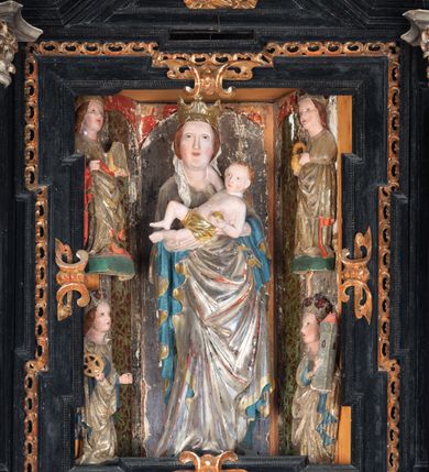 Zdjęcie nr 39: Retabulum ołtarzowe z dużą rzeźbą Matki Boskiej z Dzieciątkiem oraz mniejszymi o połowę czterema rzeźbami Świętych Dziewic umieszczonymi w prostopadłościennej szafie na rzucie trapezu (z ukośnie ustawionymi ściankami bocznymi). Rzeźby pełnoplastyczne, ścięte z tyłu, drążone, ustawione na cokolikach. Pośrodku figura Matki Boskiej w stylu gotyku międzynarodowego; zwrócona en face, w delikatnym kontrapoście, o esowato wygiętej sylwetce, podtrzymuje na obu rękach wpółleżące Dzieciatko. Twarz owalna z podwójnym podbródkiem, rysy twarzy płytko rzeźbione, delikatne, długi, prosty nos. Włosy upięte z tyłu. Maria ubrana w srebrzoną suknię z tkaniną drapowaną po środku w trzy fałdy misowe oraz złocony płaszcz podbity na niebieską podszewką, spływający od tyłu głowy na ramiona i boki, w układzie kaskadowym. Na głowie korona otwarta. Dzieciatko wpółleżące, zwrócone en trois quarts w prawo, prawą ręka ujmuje Matkę za szyję, w lewej trzyma złotą kulę. Twarz okrągła, duże uszy, włosy krótkie, kręcone. W partii bioder przepasany ściśle przylegającą, złotą tkaniną, delikatnie drapowaną. Na lewej ściance szafy u góry figurka św. Cecylii, zwróconej en face, o esowato wygiętej sylwetce, w lewej ręce, opartej na biodrze trzyma piszczałki, prawa wyciągnięta do przodu. Twarz okrągła o pełnych policzkach i płytko rzeźbionych rysach twarzy, włosy długie, falujące fakturowane, spływające przez ramiona na plecy. Ubrana w srebrzoną suknię oraz złocony płaszcz z czerwoną podszewką, spięty na piersi fibulą, z obfitą draperią przewieszoną przez ramiona, opadająca na froncie fałdami misowymi oraz spływającymi kaskadami od ramion. Na głowie blok drewna z namalowaną koroną otwartą.Na lewej ściance u dołu figura św. Katarzyny Aleksandryjskiej, zwróconej en face, w prawej ręce podtrzymuje koło, lewą wyciąga do przodu. Twarz okrągła, policzki pełne, o wysokim czole, nos duży, oczy duże delikatnie zarysowane. Włosy falowane, fakturowane, spływają na plecy. Święta ubrana w srebrzona suknię przepasaną w talii oraz złocony płaszcz spięty broszą na piersi, z obfitą draperią przewieszoną przez ramiona, opadająca na froncie misowymi fałdami i spływającymi kaskadami od ramion. Na głowie blok drewna z namalowaną koroną otwartą. Na prawej ściance u góry figura św. Doroty, zwrócona en face w delikatnym kontrapoście, prawa ręką podtrzymuje koszyk, lewą wskazuje na niego. Twarz owalna, pełna, delikatne rysy, wąski zadarty nos. Włosy falowane, fakturowane, opadają na tył głowy. Ubrana w złotą suknię, delikatnie drapowaną u dołu, oraz srebrzony płaszcz podbity czerwoną podszewką, spięty na piersi i układający się z przodu w fałdy misowe. Na głowie blok drewna z namalowaną koroną otwartą. Na prawej ściance u dołu figura św. Barbary, zwróconej en face, o esowato przegiętej sylwetce, obiema rękami przytrzymuje opartą na lewym ramieniu wieżę. Twarz owalna, pełna, delikatne rysy, wąski zadarty nos. Włosy falowane, fakturowane, opadają na tył głowy. Ubrana w suknię i srebrzony płaszcz z niebieską podszewką, spięty na piersi fibulą, przerzucony przez ramiona z obfitą partią materiału układającą się z przodu w fałdy misowe. Na głowie blok drewna z namalowaną koroną otwartą. Karnacje w tonacji naturalnej, szaty srebrzone i złocone.