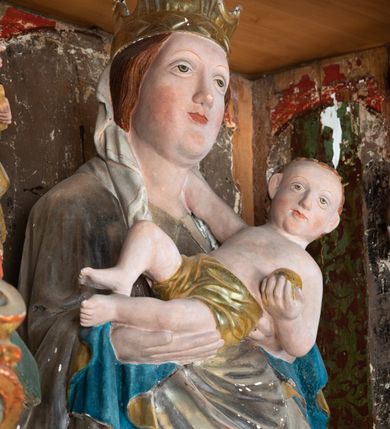 Zdjęcie nr 10: Retabulum ołtarzowe z dużą rzeźbą Matki Boskiej z Dzieciątkiem oraz mniejszymi o połowę czterema rzeźbami Świętych Dziewic umieszczonymi w prostopadłościennej szafie na rzucie trapezu (z ukośnie ustawionymi ściankami bocznymi). Rzeźby pełnoplastyczne, ścięte z tyłu, drążone, ustawione na cokolikach. Pośrodku figura Matki Boskiej w stylu gotyku międzynarodowego; zwrócona en face, w delikatnym kontrapoście, o esowato wygiętej sylwetce, podtrzymuje na obu rękach wpółleżące Dzieciatko. Twarz owalna z podwójnym podbródkiem, rysy twarzy płytko rzeźbione, delikatne, długi, prosty nos. Włosy upięte z tyłu. Maria ubrana w srebrzoną suknię z tkaniną drapowaną po środku w trzy fałdy misowe oraz złocony płaszcz podbity na niebieską podszewką, spływający od tyłu głowy na ramiona i boki, w układzie kaskadowym. Na głowie korona otwarta. Dzieciatko wpółleżące, zwrócone en trois quarts w prawo, prawą ręka ujmuje Matkę za szyję, w lewej trzyma złotą kulę. Twarz okrągła, duże uszy, włosy krótkie, kręcone. W partii bioder przepasany ściśle przylegającą, złotą tkaniną, delikatnie drapowaną. Na lewej ściance szafy u góry figurka św. Cecylii, zwróconej en face, o esowato wygiętej sylwetce, w lewej ręce, opartej na biodrze trzyma piszczałki, prawa wyciągnięta do przodu. Twarz okrągła o pełnych policzkach i płytko rzeźbionych rysach twarzy, włosy długie, falujące fakturowane, spływające przez ramiona na plecy. Ubrana w srebrzoną suknię oraz złocony płaszcz z czerwoną podszewką, spięty na piersi fibulą, z obfitą draperią przewieszoną przez ramiona, opadająca na froncie fałdami misowymi oraz spływającymi kaskadami od ramion. Na głowie blok drewna z namalowaną koroną otwartą.Na lewej ściance u dołu figura św. Katarzyny Aleksandryjskiej, zwróconej en face, w prawej ręce podtrzymuje koło, lewą wyciąga do przodu. Twarz okrągła, policzki pełne, o wysokim czole, nos duży, oczy duże delikatnie zarysowane. Włosy falowane, fakturowane, spływają na plecy. Święta ubrana w srebrzona suknię przepasaną w talii oraz złocony płaszcz spięty broszą na piersi, z obfitą draperią przewieszoną przez ramiona, opadająca na froncie misowymi fałdami i spływającymi kaskadami od ramion. Na głowie blok drewna z namalowaną koroną otwartą. Na prawej ściance u góry figura św. Doroty, zwrócona en face w delikatnym kontrapoście, prawa ręką podtrzymuje koszyk, lewą wskazuje na niego. Twarz owalna, pełna, delikatne rysy, wąski zadarty nos. Włosy falowane, fakturowane, opadają na tył głowy. Ubrana w złotą suknię, delikatnie drapowaną u dołu, oraz srebrzony płaszcz podbity czerwoną podszewką, spięty na piersi i układający się z przodu w fałdy misowe. Na głowie blok drewna z namalowaną koroną otwartą. Na prawej ściance u dołu figura św. Barbary, zwróconej en face, o esowato przegiętej sylwetce, obiema rękami przytrzymuje opartą na lewym ramieniu wieżę. Twarz owalna, pełna, delikatne rysy, wąski zadarty nos. Włosy falowane, fakturowane, opadają na tył głowy. Ubrana w suknię i srebrzony płaszcz z niebieską podszewką, spięty na piersi fibulą, przerzucony przez ramiona z obfitą partią materiału układającą się z przodu w fałdy misowe. Na głowie blok drewna z namalowaną koroną otwartą. Karnacje w tonacji naturalnej, szaty srebrzone i złocone.