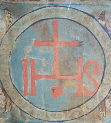 Zdjęcie nr 1: W kształcie wydłużonego ośmioboku o czterech przeciwległych (po przekątnej) bokach wklęsłych. Pośrodku na błękitnym tle duży kolisty medalion, w polu którego duże czerwone litery IHS z krzyżem oraz motywem serca poniżej. Obramienie medalionu wypełnione motywem wolut. Wokół medalionu główki aniołków ze skrzydłami. Kolorystyka pociemniała. 