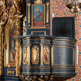 Zdjęcie nr 1: Ambona przyścienna, wisząca, z dostępem przez drzwi od strony zakrystii. Kosz wieloboczny, na cokole, z podwieszeniem w postaci ośmiu kabłąków, zakończonych szyszką. Ścianki kosza wydzielone kolumienkami podtrzymującymi wyłamane na ich osi belkowanie z silnie wysuniętym gzymsem tworzącym parapet. W polach nisze z płaskorzeźbionymi przedstawieniami ewangelistów. Po prawej stronie do kosza dobudowany ćwierćkolisty podest z pełną balustradą. Zaplecek wąski, ujęty dwiema kolumienkami stojącymi na wspornikach, podtrzymującymi imposty, na których stoją wazoniki. W dolnej części płycina. W polu obraz w formie stojącego prostokąta, ujęty ramą zakończoną muszlą, z przedstawieniem Chrystusa w typie Salvator Mundi. Baldachim na planie ośmioboku, w formie belkowania, na którym ustawione są kabłąki, podtrzymujące figurę anioła grającego na trąbie. Na podniebiu baldachimu figura gołębicy Ducha Świętego w glorii promienistej. Struktura polichromowana w kolorze niebiesko-zielonym; kolumienki, profile i ornamentyka złocone. 
