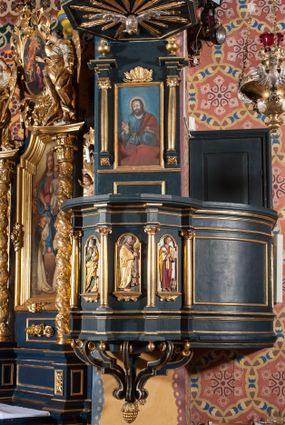 Zdjęcie nr 1: Ambona przyścienna, wisząca, z dostępem przez drzwi od strony zakrystii. Kosz wieloboczny, na cokole, z podwieszeniem w postaci ośmiu kabłąków, zakończonych szyszką. Ścianki kosza wydzielone kolumienkami podtrzymującymi wyłamane na ich osi belkowanie z silnie wysuniętym gzymsem tworzącym parapet. W polach nisze z płaskorzeźbionymi przedstawieniami ewangelistów. Po prawej stronie do kosza dobudowany ćwierćkolisty podest z pełną balustradą. Zaplecek wąski, ujęty dwiema kolumienkami stojącymi na wspornikach, podtrzymującymi imposty, na których stoją wazoniki. W dolnej części płycina. W polu obraz w formie stojącego prostokąta, ujęty ramą zakończoną muszlą, z przedstawieniem Chrystusa w typie Salvator Mundi. Baldachim na planie ośmioboku, w formie belkowania, na którym ustawione są kabłąki, podtrzymujące figurę anioła grającego na trąbie. Na podniebiu baldachimu figura gołębicy Ducha Świętego w glorii promienistej. Struktura polichromowana w kolorze niebiesko-zielonym; kolumienki, profile i ornamentyka złocone. 
