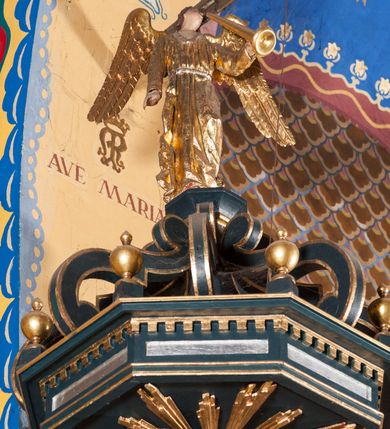 Zdjęcie nr 6: Ambona przyścienna, wisząca, z dostępem przez drzwi od strony zakrystii. Kosz wieloboczny, na cokole, z podwieszeniem w postaci ośmiu kabłąków, zakończonych szyszką. Ścianki kosza wydzielone kolumienkami podtrzymującymi wyłamane na ich osi belkowanie z silnie wysuniętym gzymsem tworzącym parapet. W polach nisze z płaskorzeźbionymi przedstawieniami ewangelistów. Po prawej stronie do kosza dobudowany ćwierćkolisty podest z pełną balustradą. Zaplecek wąski, ujęty dwiema kolumienkami stojącymi na wspornikach, podtrzymującymi imposty, na których stoją wazoniki. W dolnej części płycina. W polu obraz w formie stojącego prostokąta, ujęty ramą zakończoną muszlą, z przedstawieniem Chrystusa w typie Salvator Mundi. Baldachim na planie ośmioboku, w formie belkowania, na którym ustawione są kabłąki, podtrzymujące figurę anioła grającego na trąbie. Na podniebiu baldachimu figura gołębicy Ducha Świętego w glorii promienistej. Struktura polichromowana w kolorze niebiesko-zielonym; kolumienki, profile i ornamentyka złocone. 
