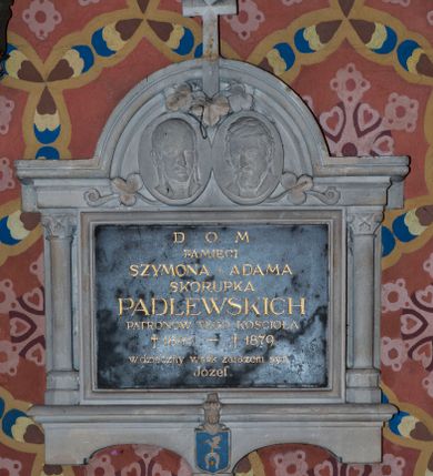 Zdjęcie nr 1: Marmurowa tablica w kształcie leżącego prostokąta, ujęta kamienną, architektoniczną obudową w formie aediculi. Tablica u dołu zamknięta profilowanym gzymsem, z wspornikiem pośrodku, na którym znajduje się tarcza z godłem herbowym Ślepowron. Pole tarczy szrafowane poziomo i pomalowane na błękitny kolor, zaś elementy godła złocone (krzyże i pierścień). 
Tarcza nakryta hełmem prętowym z utrąconym klejnotem. Tablica flankowana korynckimi kolumienkami dźwigającymi belkowanie z gzymsem wyłamanym pośrodku półkoliście, zwieńczonym krzyżem. W podłuczu dwa medaliony z płaskorzeźbionymi wizerunkami zmarłych, dekorowane ornamentem roślinnym. W polu płyty inskrypcja „D(EO) O(PTIMO) M(AXIMO) / PAMIĘCI / SZYMONA I ADAMA / SKORUPKA / PADLEWSKICH / PATRONÓW TEGO KOŚCIOŁA / + 1841 – +1879 / wdzięczny wnuk zarazem syn / Józef”.