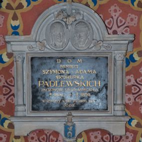 Zdjęcie nr 1: Marmurowa tablica w kształcie leżącego prostokąta, ujęta kamienną, architektoniczną obudową w formie aediculi. Tablica u dołu zamknięta profilowanym gzymsem, z wspornikiem pośrodku, na którym znajduje się tarcza z godłem herbowym Ślepowron. Pole tarczy szrafowane poziomo i pomalowane na błękitny kolor, zaś elementy godła złocone (krzyże i pierścień). 
Tarcza nakryta hełmem prętowym z utrąconym klejnotem. Tablica flankowana korynckimi kolumienkami dźwigającymi belkowanie z gzymsem wyłamanym pośrodku półkoliście, zwieńczonym krzyżem. W podłuczu dwa medaliony z płaskorzeźbionymi wizerunkami zmarłych, dekorowane ornamentem roślinnym. W polu płyty inskrypcja „D(EO) O(PTIMO) M(AXIMO) / PAMIĘCI / SZYMONA I ADAMA / SKORUPKA / PADLEWSKICH / PATRONÓW TEGO KOŚCIOŁA / + 1841 – +1879 / wdzięczny wnuk zarazem syn / Józef”.
