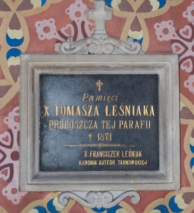 Zdjęcie nr 1: Tablica z czarnego marmuru w formie leżącego prostokąta, ujęta profilowaną ramą z piaskowca, zwieńczoną wolutowym szczytem z krzyżem. W polu inskrypcja „Pamięci / X(IĘDZA) TOMASZA LEŚNIAKA / PROBOSZCZA TEJ PARAFII / + 1871 / X(IĘDZA) FRANCISZEK LEŚNIAK / KANONIK KATEDR(Y) TARNOWSKIEJ”.