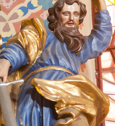 Zdjęcie nr 3: Pełnoplastyczna rzeźba ustawiona na nieregularnej podstawie. Święty ukazany frontalnie, w kontrapoście, z ugiętą lewą nogą oraz pochyloną głową. Lewą rękę unosi wysoko, z wskazującym gestem dłoni, prawą wyciąga w dół, w dłoni trzyma srebrzony miecz, skierowany ostrzem w dół. Twarz ma pociągłą, szczupłą, o migdałowatych oczach, dużym nosie i rozchylonych, pełnych ustach. Okolona jest gęstą, skręconą brodą opadającą na pierś oraz krótkimi, falistymi włosami. Święty ubrany jest w niebieską tunikę, przylegającą do ciała i silnie drapowaną, przepasaną w talii oraz złocony płaszcz przewiązany przez prawe ramię i zawinięty na lewej nodze, na stopach ma złocone buty. Polichromia ciała naturalistyczna.
