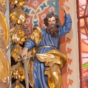 Zdjęcie nr 1: Pełnoplastyczna rzeźba ustawiona na nieregularnej podstawie. Święty ukazany frontalnie, w kontrapoście, z ugiętą lewą nogą oraz pochyloną głową. Lewą rękę unosi wysoko, z wskazującym gestem dłoni, prawą wyciąga w dół, w dłoni trzyma srebrzony miecz, skierowany ostrzem w dół. Twarz ma pociągłą, szczupłą, o migdałowatych oczach, dużym nosie i rozchylonych, pełnych ustach. Okolona jest gęstą, skręconą brodą opadającą na pierś oraz krótkimi, falistymi włosami. Święty ubrany jest w niebieską tunikę, przylegającą do ciała i silnie drapowaną, przepasaną w talii oraz złocony płaszcz przewiązany przez prawe ramię i zawinięty na lewej nodze, na stopach ma złocone buty. Polichromia ciała naturalistyczna.
