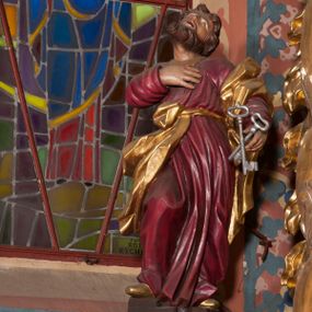 Zdjęcie nr 1: Pełnoplastyczna rzeźba ustawiona na nieregularnej podstawie. Święty ukazany frontalnie, w kontrapoście, z ugiętą prawą nogą oraz głową uniesioną i odchyloną do tyłu. Prawą rękę kładzie na piersi, w lewej nieco wyciągniętej przed siebie trzyma dwa skrzyżowane, srebrzone klucze. Twarz ma szczupłą, o oczach skierowanych w górę, dużym nosie i otwartych ustach, okoloną krótką brodą skręconą w dwa pukle oraz krótkimi, silnie kręconymi włosami. Ubrany jest w czerwoną tunikę, przepasaną w talii, silnie drapowaną, przylegającą do ciała oraz złocony płaszcz zawinięty na lewym ramieniu i zawiązany z przodu postaci, na stopach złocone buty. Polichromia ciała naturalistyczna. 

